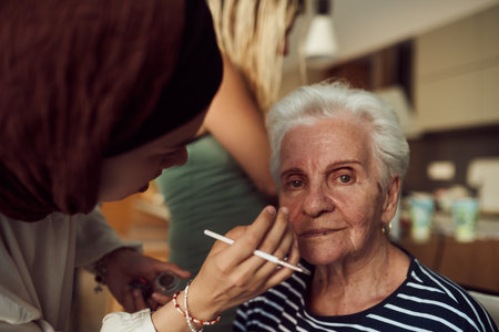 In this heartwarming real-life scene, a girl in a hijab and her sister lovingly apply makeup to their elderly grandmother, preparing her for a special family anniversary celebration, showcasing the bonds of family and cultural traditionsの写真素材