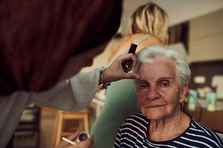 In this heartwarming real-life scene, a girl in a hijab and her sister lovingly apply makeup to their elderly grandmother, preparing her for a special family anniversary celebration, showcasing the bonds of family and cultural traditionsの写真素材