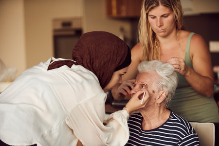 In this heartwarming real-life scene, a girl in a hijab and her sister lovingly apply makeup to their elderly grandmother, preparing her for a special family anniversary celebration, showcasing the bonds of family and cultural traditionsの写真素材