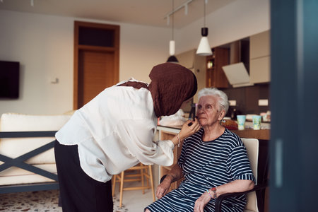 In this heartwarming real-life scene, a girl in a hijab and her sister lovingly apply makeup to their elderly grandmother, preparing her for a special family anniversary celebration, showcasing the bonds of family and cultural traditionsの写真素材