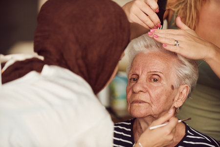 In this heartwarming real-life scene, a girl in a hijab and her sister lovingly apply makeup to their elderly grandmother, preparing her for a special family anniversary celebration, showcasing the bonds of family and cultural traditionsの写真素材