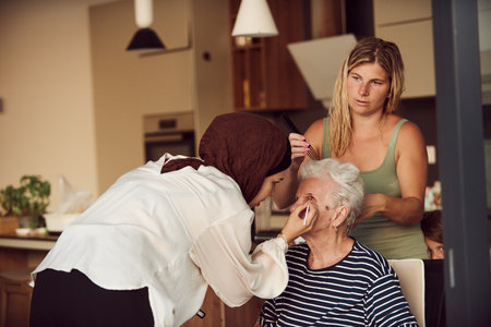 In this heartwarming real-life scene, a girl in a hijab and her sister lovingly apply makeup to their elderly grandmother, preparing her for a special family anniversary celebration, showcasing the bonds of family and cultural traditionsの写真素材