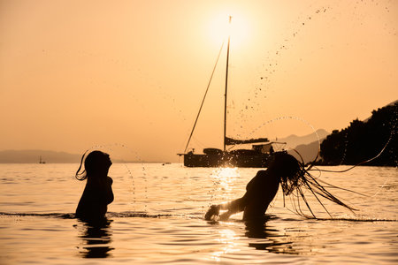 Two women flipping hair in sea at sunsetの写真素材