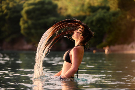 Woman flipping wet hair in water at sunsetの写真素材