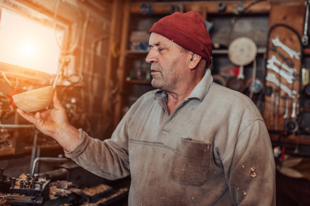 A senior man processing wooden dishes in the workshop in the traditional manual wayの写真素材