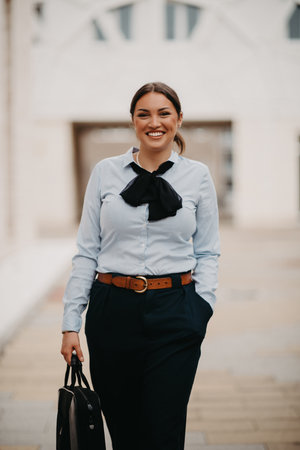 Smiling Latina businesswoman strides confidently through urban streets.