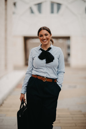 Smiling Latina businesswoman strides confidently through urban streets.の写真素材