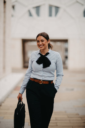 Smiling Latina businesswoman strides confidently through urban streets.の写真素材