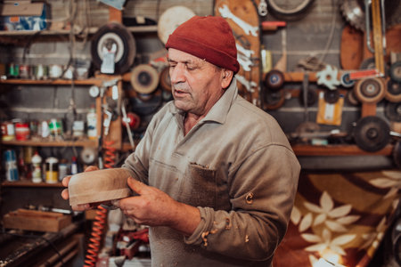 A senior man processing wooden dishes in the workshop in the traditional manual wayの写真素材