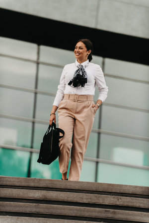 Smiling Latina businesswoman strides confidently through urban streets.の写真素材