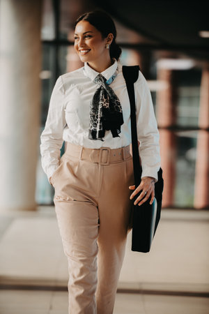 Empowered Latina businesswoman strides confidently through modern office.の写真素材