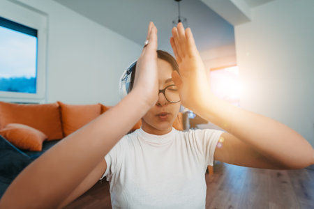 A young woman is practicing yoga and relaxing with headphones on her head in a modern apartment