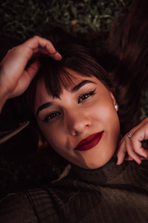 A young woman is lying on the grass, showing off her beautiful face with a serene expression. The lush greenery in the background adds to the peaceful atmosphere of the scene, making it a relaxing and idyllic moment captured in time.の写真素材