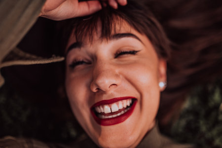 A young woman is lying on the grass, showing off her beautiful face with a serene expression. The lush greenery in the background adds to the peaceful atmosphere of the scene, making it a relaxing and idyllic moment captured in time.の写真素材