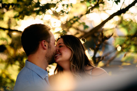 Young couple sharing a romantic kiss outdoors in warm evening sunlight, symbolizing love, intimacy,...