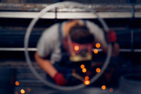 Skilled factory worker welding metal parts while wearing protective mask, gloves, and safety gear in...