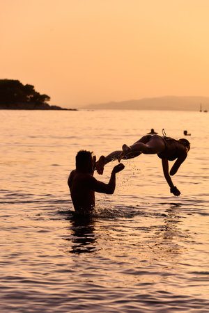 Man throwing girl into water during sunsetの写真素材