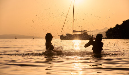 Two women flipping hair in sea at sunsetの写真素材