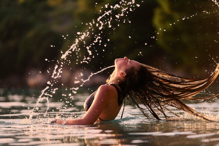 Woman flipping wet hair in water at sunset