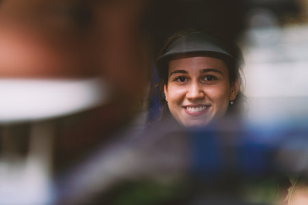 Smiling woman wearing a visor, looking at the camera, with a blurred foreground, creating a sense of mystery and anticipation, perfect for advertising or editorial use.の写真素材