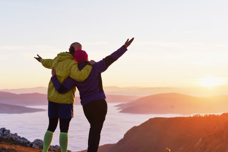 Couple celebrates sunset on a mountain peak, capturing a moment of joy and connection in the evening skyの写真素材