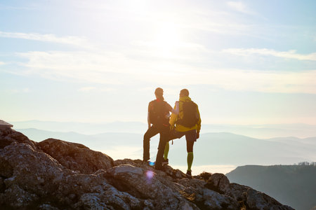 Couple enjoying breathtaking view from mountain peak during sunset on a clear dayの写真素材