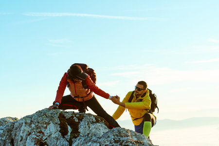 Two hikers climbing a rocky peak under a clear blue sky during early morning hours in the mountainsの写真素材