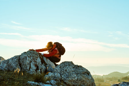 Hiker climbs rocky terrain at sunset in mountainous landscape under clear skyの写真素材