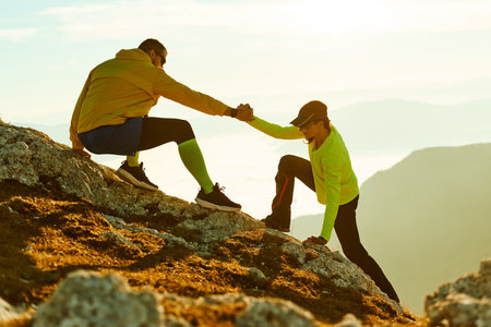 Two climbers assist each other while scaling a rocky mountain at sunrise. The golden light...