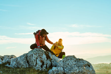 Two hikers climbing a rocky peak under a clear blue sky during early morning hours in the mountainsの写真素材