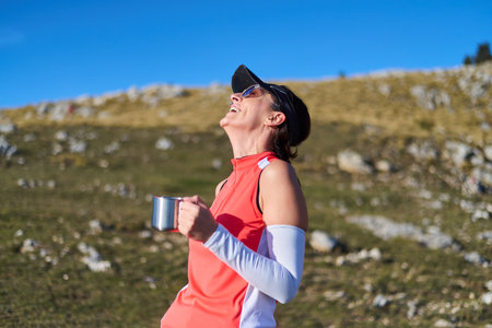 Enjoying a warm drink and smiling during a mountain run on a sunny dayの写真素材