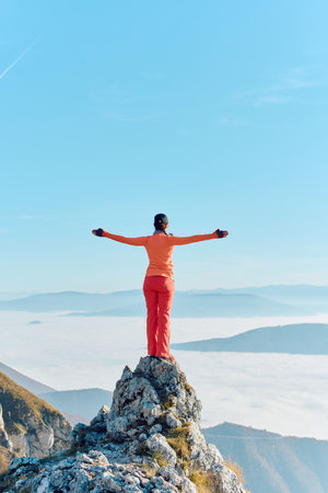 Stunning view from a mountain peak with a person in bright orange clothing embracing the open sky at sunriseの写真素材