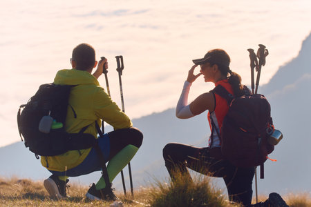 Couple enjoys stunning view while hiking in mountains during sunrise with clouds belowの写真素材