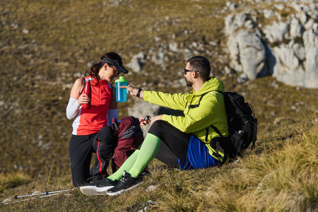 Hikers take a break on a mountain trail to hydrate and enjoy the fresh air during a sunny dayの写真素材