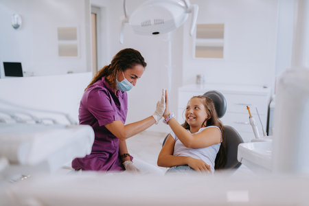 A caring dentist engages in a joyful conversation and entertains a little girl after a dental treatment, creating a child friendly and pleasant atmosphere in the dental office.の写真素材