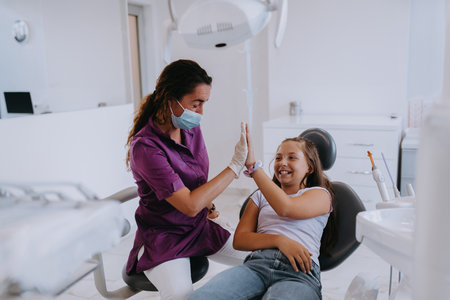 A caring dentist engages in a joyful conversation and entertains a little girl after a dental treatment, creating a child friendly and pleasant atmosphere in the dental office.の写真素材