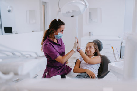 A caring dentist engages in a joyful conversation and entertains a little girl after a dental treatment, creating a child friendly and pleasant atmosphere in the dental office.の写真素材
