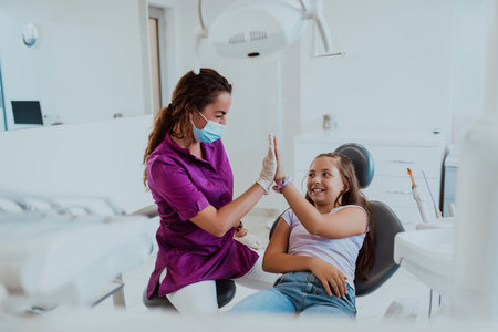 A caring dentist engages in a joyful conversation and entertains a little girl after a dental treatment, creating a child friendly and pleasant atmosphere in the dental office.の写真素材