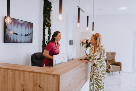 A beautiful blonde woman conversing with the dental clinic receptionist, scheduling an appointment for dental treatment with a bright smileの写真素材
