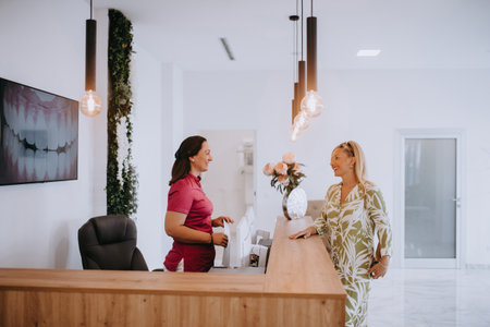 A beautiful blonde woman conversing with the dental clinic receptionist, scheduling an appointment for dental treatment with a bright smileの写真素材