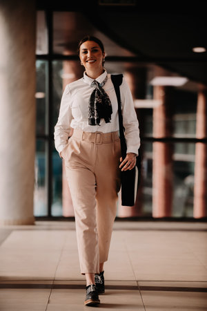 Empowered Latina businesswoman strides confidently through modern office.の写真素材