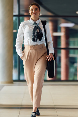 Empowered Latina businesswoman strides confidently through modern office.の写真素材