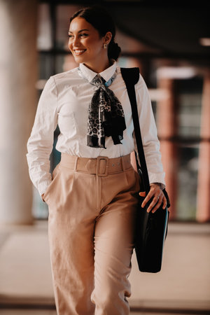 Empowered Latina businesswoman strides confidently through modern office.の写真素材