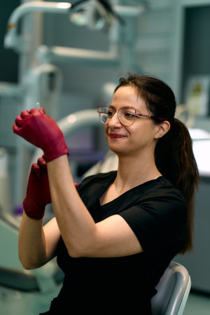 Female Medical Professional In Red Gloves Inspecting Instrument In Modern Clinicの写真素材