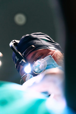 Surgeon At Work Wearing Mask And Headlamp In Operating Room During Procedureの写真素材