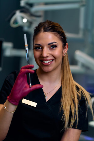 Confident Dental Professional Holding Syringe, Smiling At Camera In Clean Clinic Setting