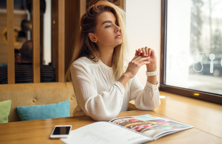 Beautiful girl looks out the window, sitting in a cafeの写真素材
