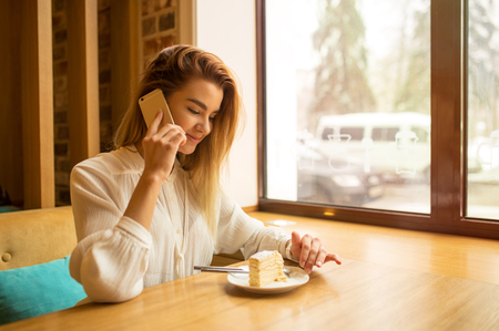 A girl is sitting in a cafe and using a smartphone, typing on the phoneの写真素材