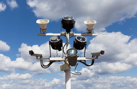 Two security cameras, floodlights and loudspeakers on blue sky background