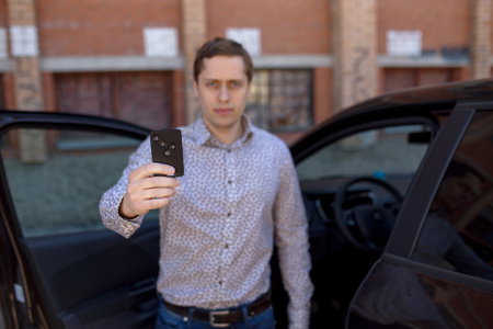 young owner man standing near a car and holding a car alarm key. Man blur effect.の写真素材